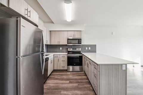 A modern kitchen with a stainless steel refrigerator and wooden flooring.