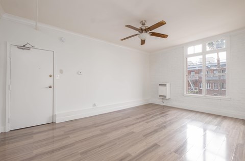 A room with a ceiling fan and a window showing a view of a building outside at Mariposa Willows Apartments, California