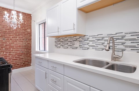 A kitchen with white cabinets and a brick wall at Mariposa Willows Apartments, Los Angeles