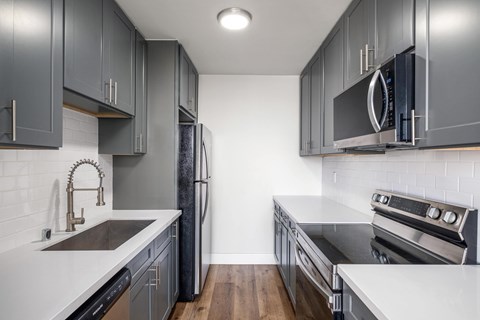 A modern kitchen with dark grey cabinets and stainless steel appliances.