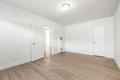 A room with white walls and wooden flooring with three doors.