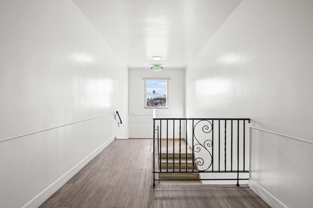 A staircase with a black railing and wooden steps leads to a balcony with a view of a building.
