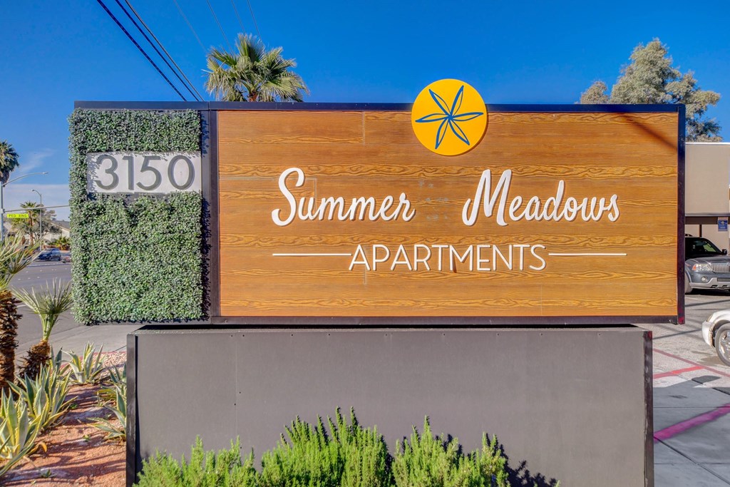 A wooden sign for Summer Meadows Apartments is displayed in front of a building.