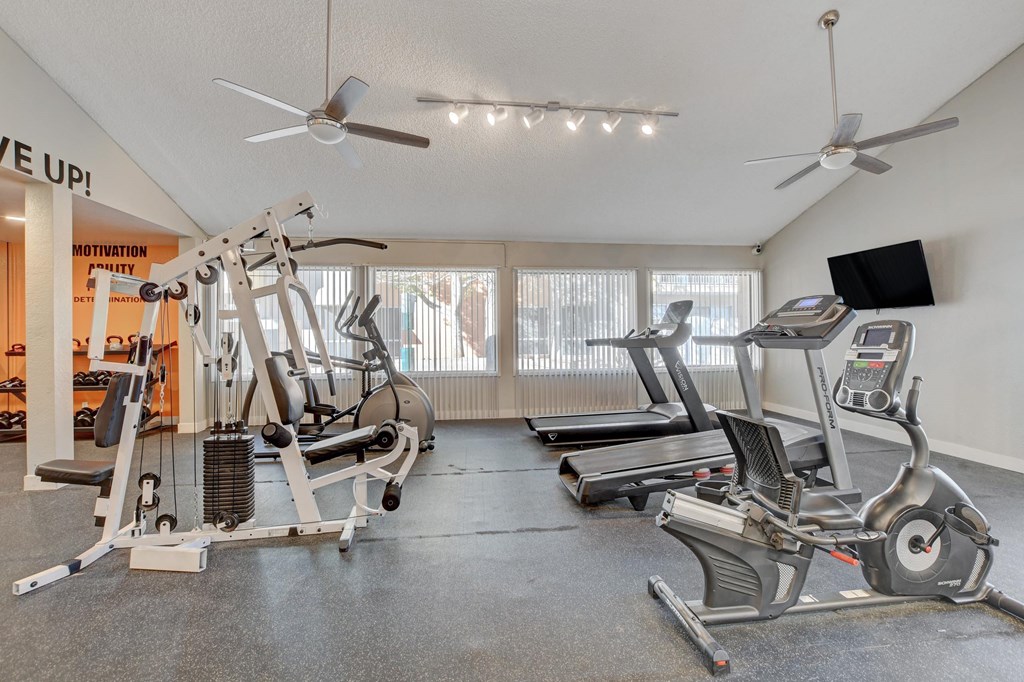 A gym with a variety of equipment including treadmills, elliptical machines, and a weight bench.