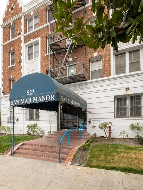 A white building with a blue awning that says San Mar Manor.