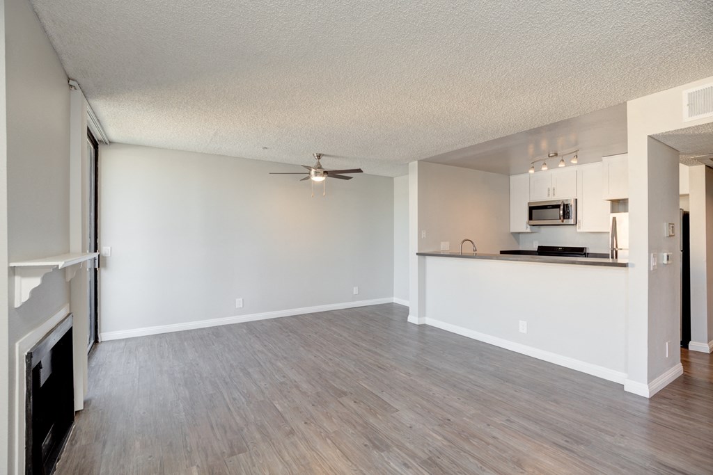 an empty living room with a kitchen and a ceiling fan