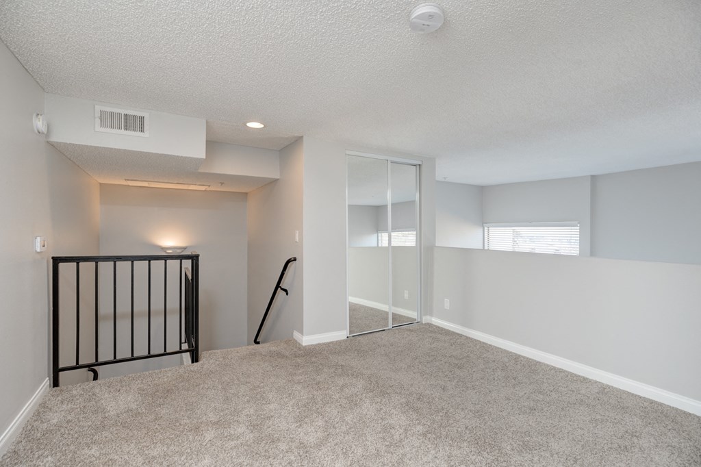 the upstairs loft of an apartment with a staircase and carpeted flooring