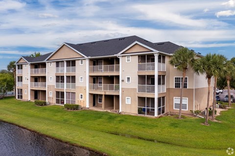 an apartment building with palm trees in front of a lake at Village Lakes, Orlando, FL, 32808