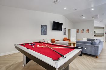 A pool table is in the middle of a room with a couch and a television.