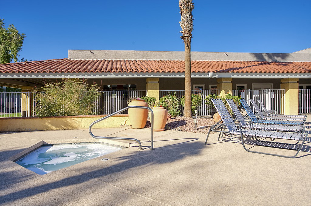A pool area with a hot tub, chairs, and a palm tree.
