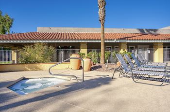 A pool area with a hot tub, chairs, and a palm tree.
