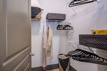 A closet with clothes hanging and a basket on the floor.