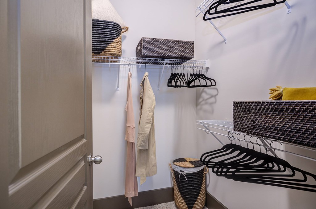 A closet with clothes hanging and a basket on the floor.