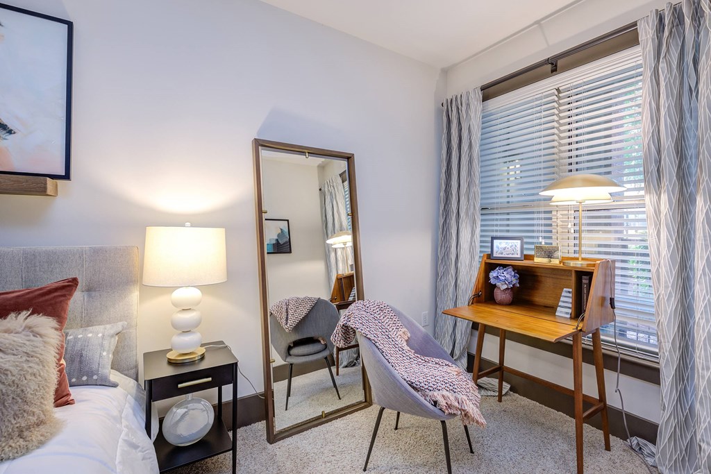 A bedroom with a bed, a chair, a desk, and a mirror.