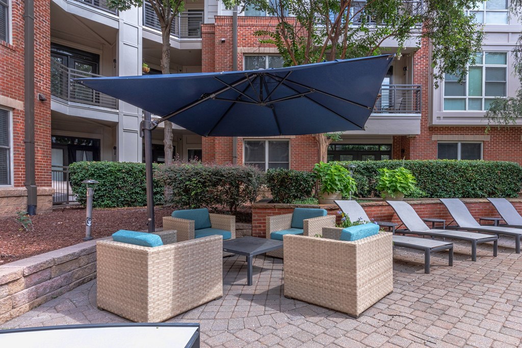 A patio with a large umbrella and wicker furniture.