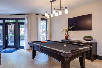 A pool table with a television on the wall and a plant on the side table.