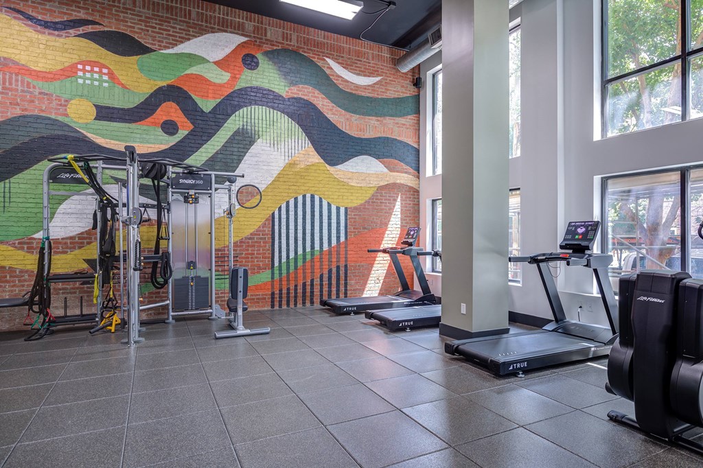 A gym with treadmills and a colorful mural on the wall.
