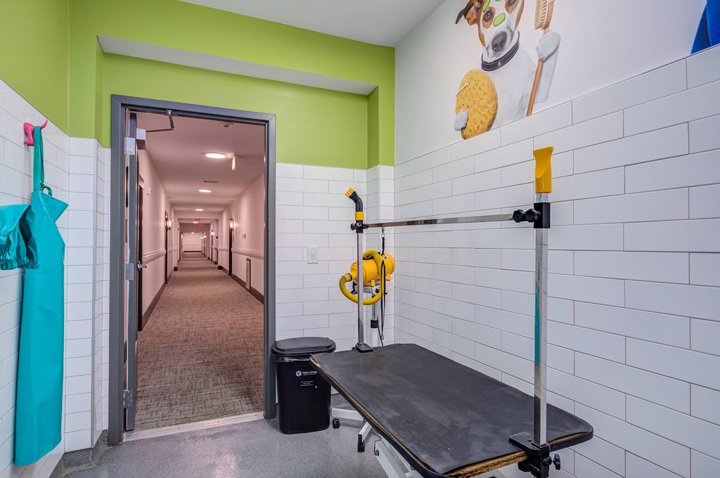 A room with a white tiled wall and a black trash can.
