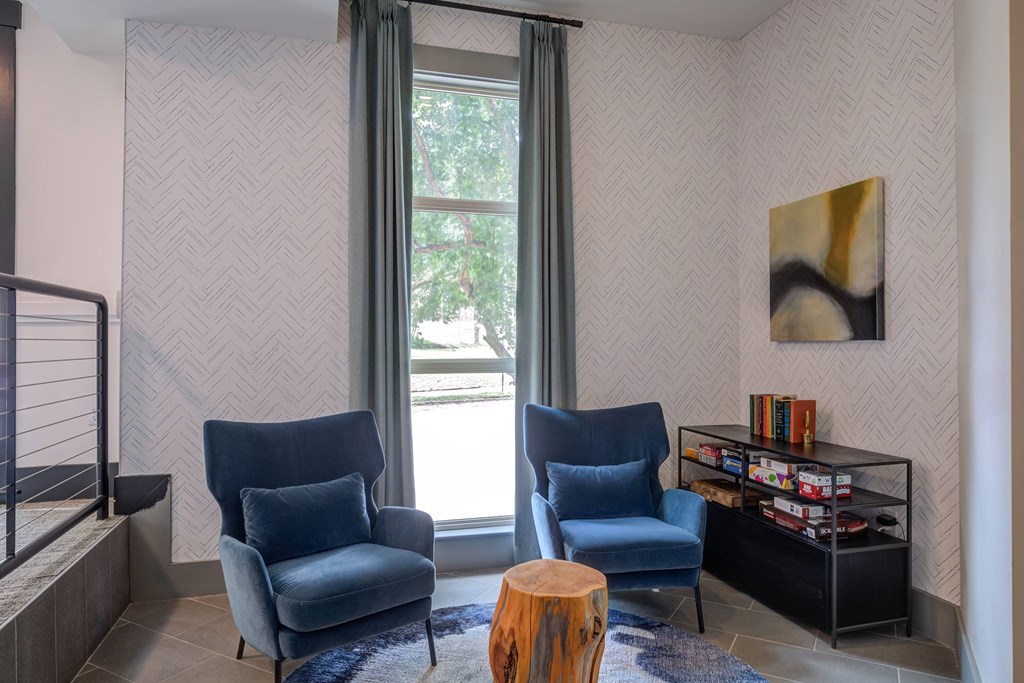 Two blue chairs are in front of a window with a grey curtain.