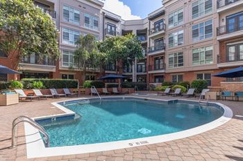 A swimming pool surrounded by lounge chairs and umbrellas in front of apartment buildings.