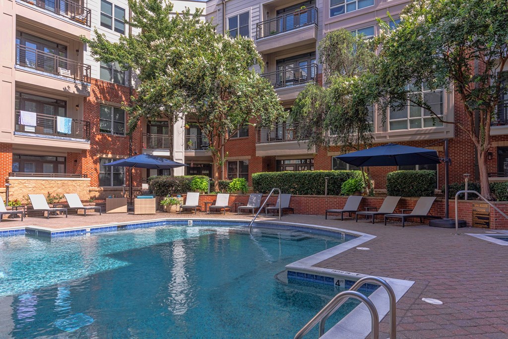 A swimming pool surrounded by lounge chairs and umbrellas in front of apartment buildings.