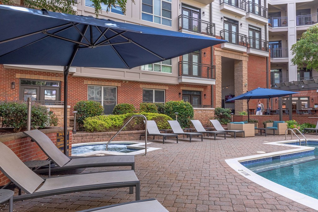 A pool area with lounge chairs and umbrellas in front of a brick building.