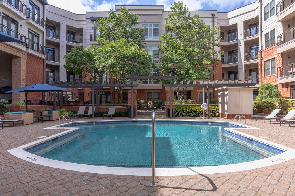 A swimming pool surrounded by a brick patio and lounge chairs.