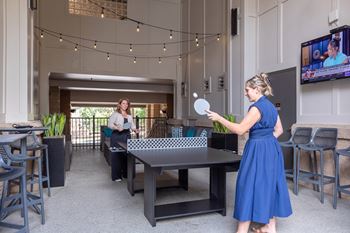 A woman in a blue dress is playing ping pong in a room with a TV on the wall.