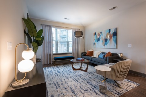 A living room with a blue rug and a large painting on the wall.