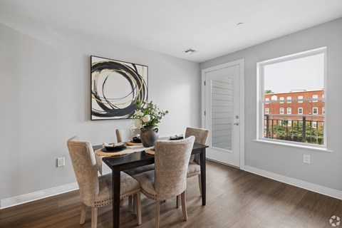 A dining room with a table set for two and a view of a building outside the window.