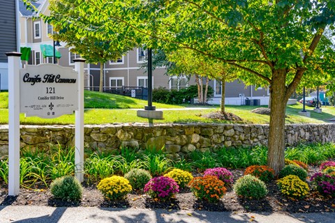 The entrance to a community with a sign that reads "Congrats 121" and a stone wall with colorful flowers in front.