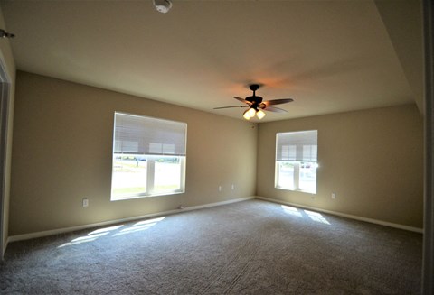 A room with a ceiling fan and two windows.