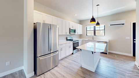 A modern kitchen with a stainless steel refrigerator and wooden flooring.
