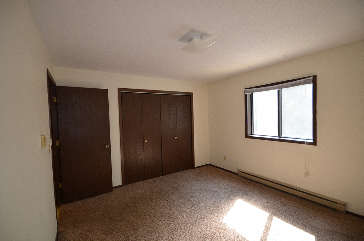 A room with brown carpet, two brown doors and a window.