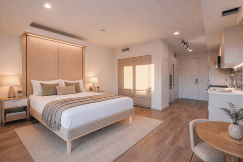 A bedroom with a large bed and a dining area in the background.