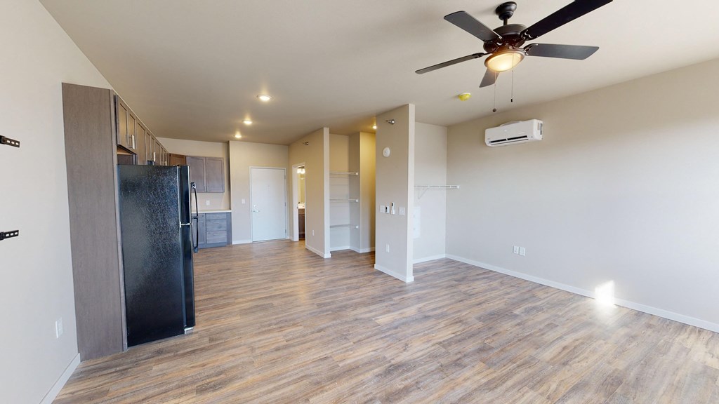 an empty living room with a kitchen and a ceiling fan