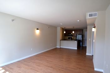 an empty living room with a kitchen in the background