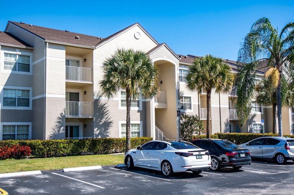 an apartment building with palm trees and cars parked in front of it
