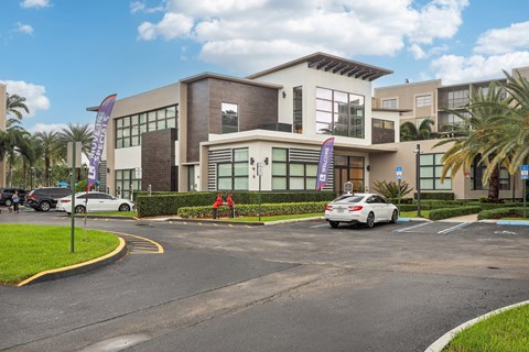 A white car is parked in front of a building with a purple banner.