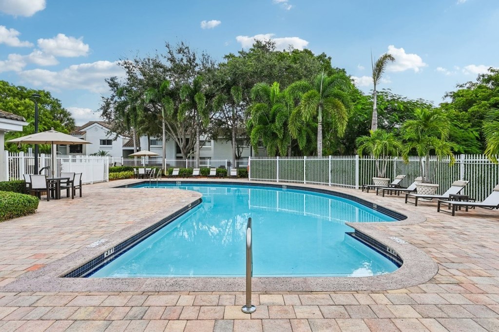 A swimming pool surrounded by a brick patio and lounge chairs.