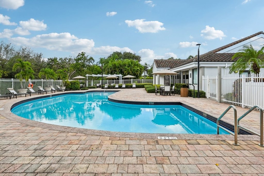 A swimming pool surrounded by a brick patio and a white fence.