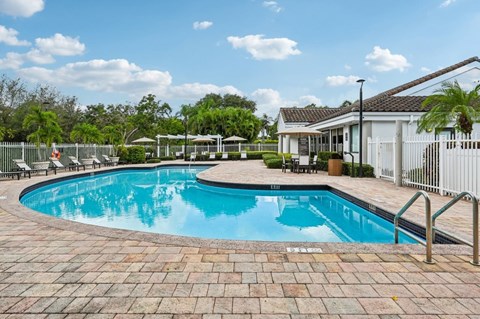 A swimming pool surrounded by a brick patio and a white fence.