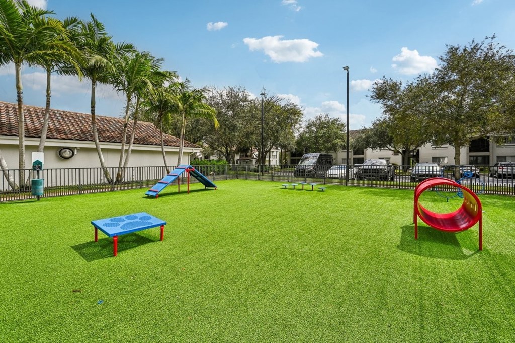 A playground with a blue and red slide, a red and blue swing set, and a green lawn.