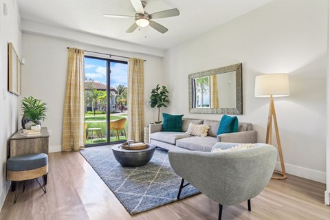 A living room with a grey sofa, a round table, a wooden floor, and a ceiling fan.