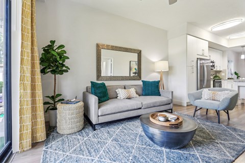 A living room with a grey couch, a round coffee table, and a mirror on the wall.