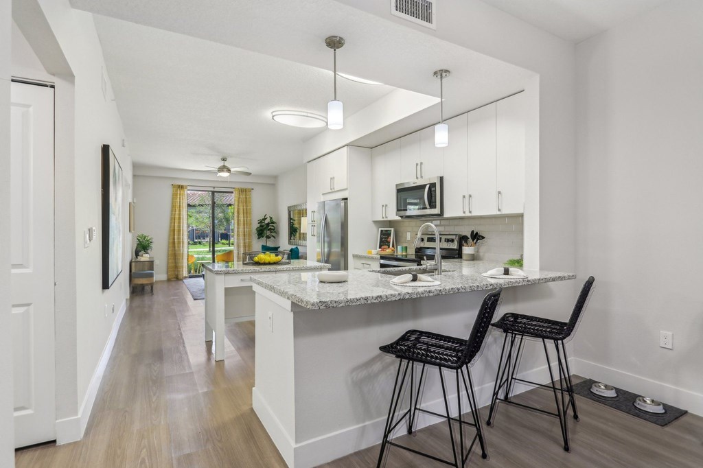 A kitchen with a white counter and black barstools.