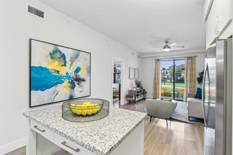 A kitchen with a large painting on the wall and a bowl of bananas on the island.