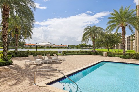 A pool surrounded by palm trees and lounge chairs.