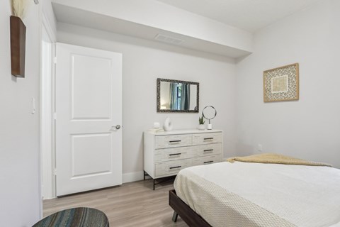 A white bedroom with a bed, dresser, and mirror.