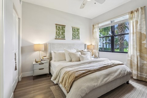 A bedroom with a large bed and a window overlooking a palm tree.